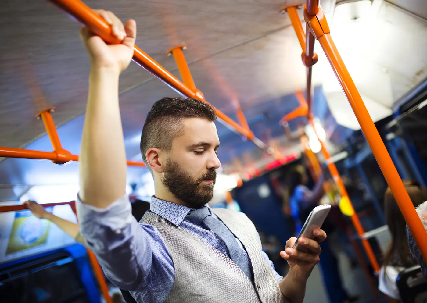 Fahrgast hält sich an Haltestange fest, schaut aber aufs Smartphone