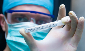 Ein Mann in einem Labor trägt Schutzmaske und Schutzbrille und  hält ein Reagenzglas  mit der Aufschrift "Corona Virus".
