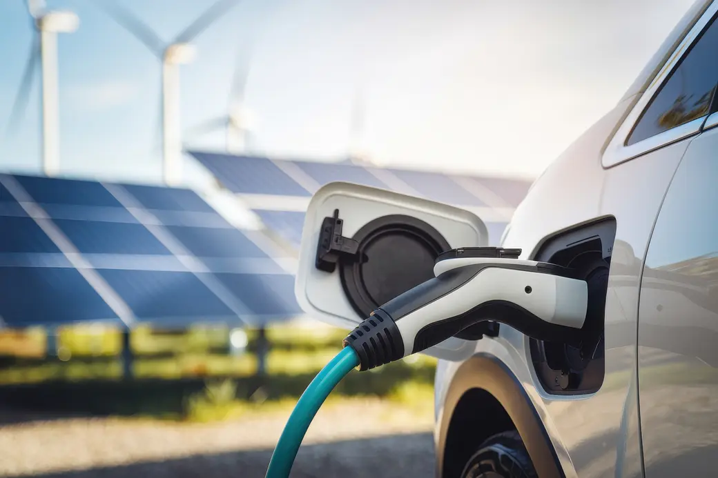 E-Auto wird geladen, im Hintergrund Solar und Windräder